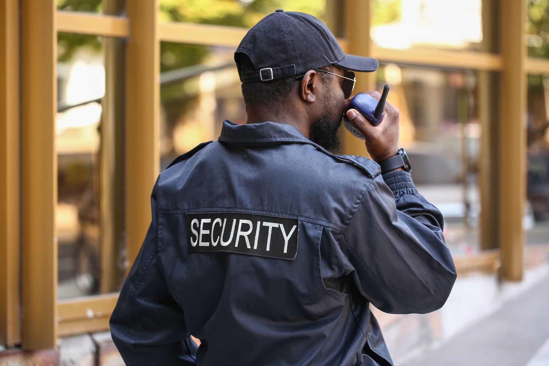 Security guard in dark jacket speaking into a handheld radio outside a building