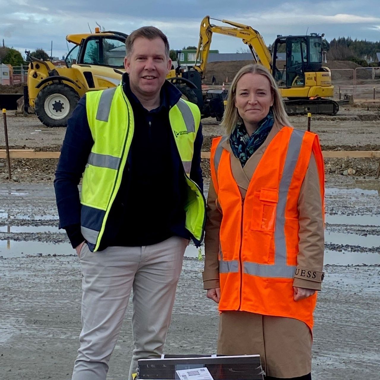 Two people in safety vests at a construction site with machinery in the background.