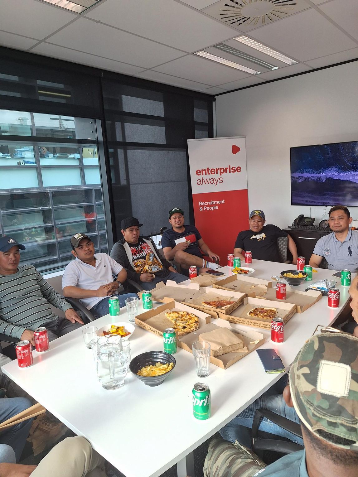 Group of people at a table eating pizza and drinks in an office setting, with an 
