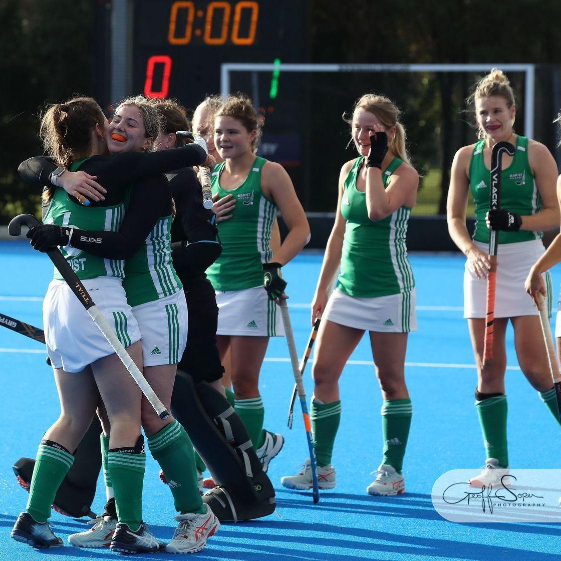 Field hockey players in green and white celebrate on a blue field; scoreboard reads 0:00.