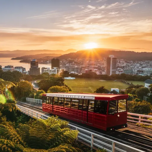 Red cable car ascending track at sunset, overlooking Wellington city and harbor.