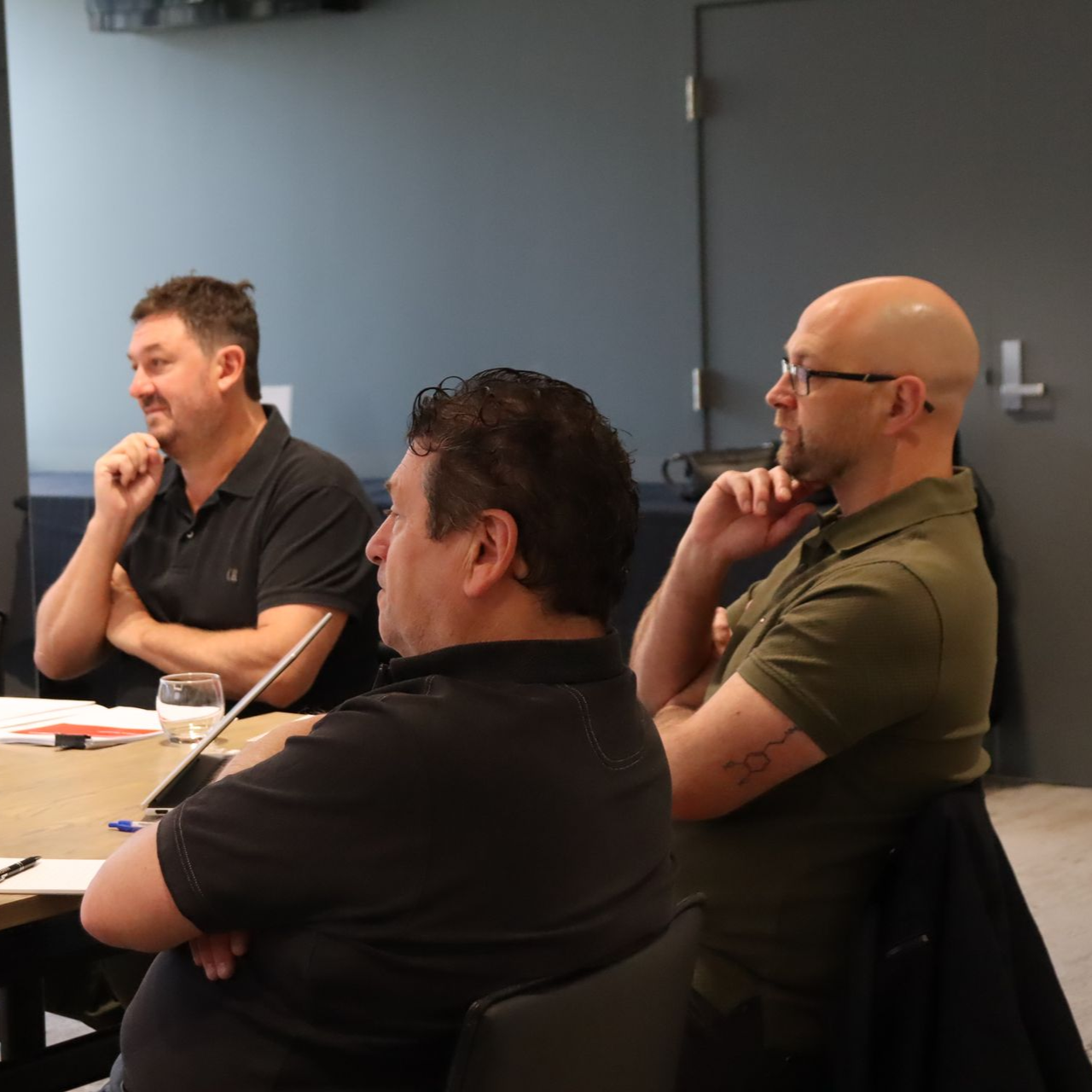 Three people seated at a conference table, listening attentively in a meeting room.