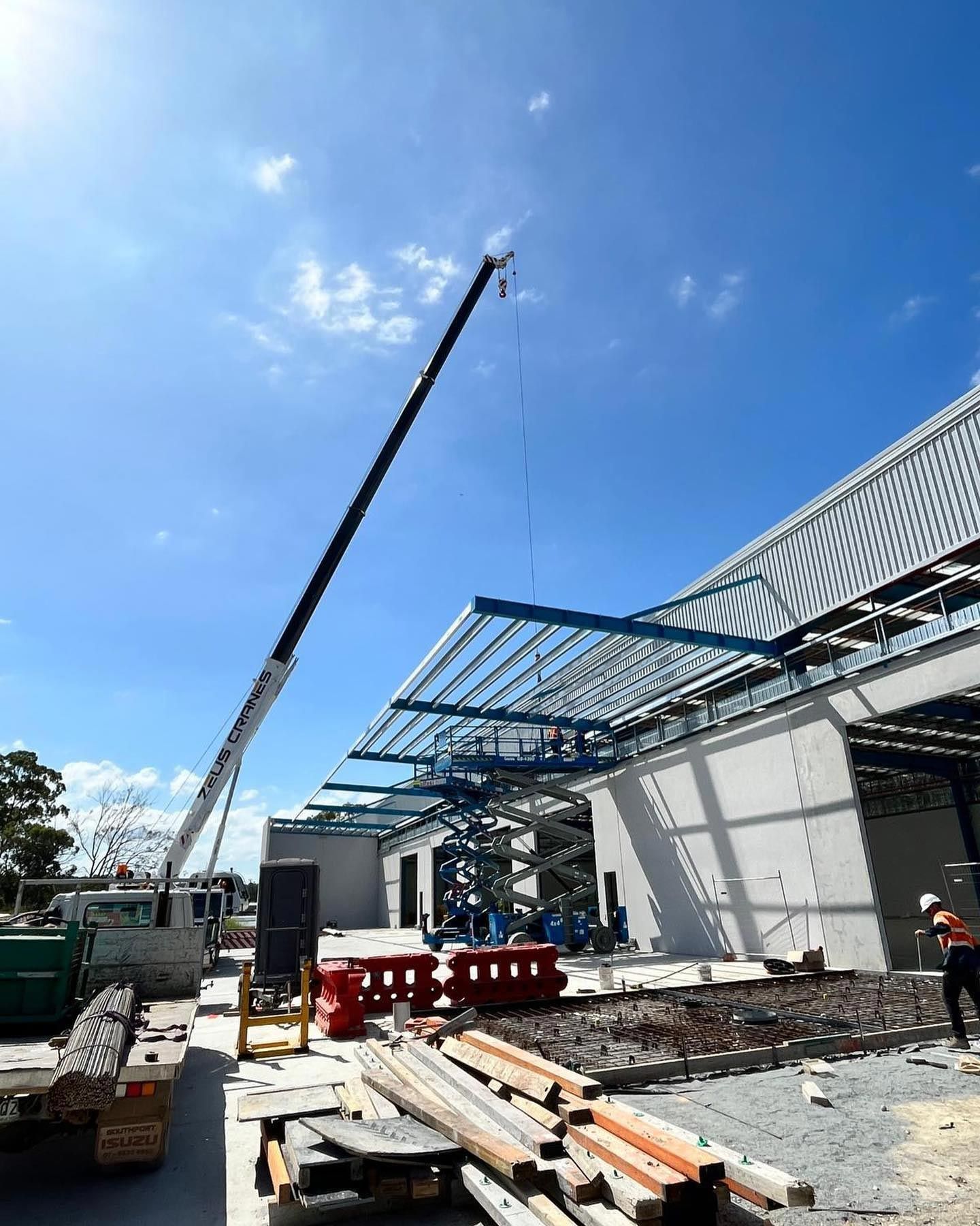 Crane lifting steel roof beams into place at a commercial construction site.