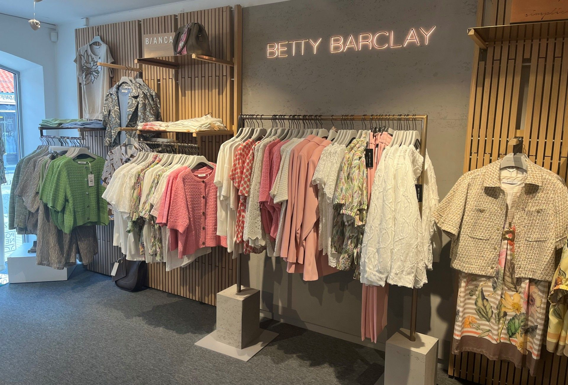 Tøjstativ i en butik med mønstrede skjorter og skiltet 