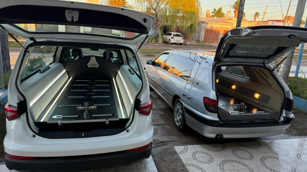 Dos coches compactos con las puertas traseras abiertas, mostrando un sistema de almacenamiento de carga personalizado en una entrada de garaje al atardecer.