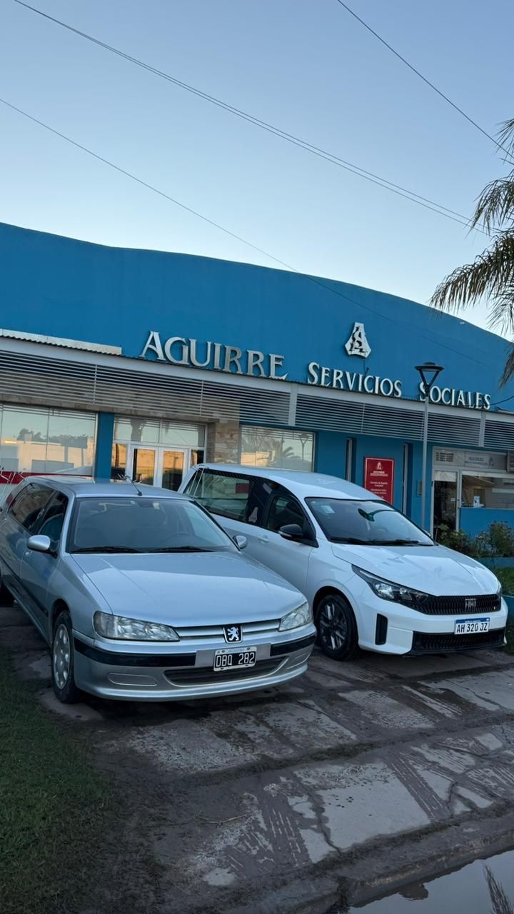 Dos coches aparcados frente al taller de neumáticos y automóviles Aguirre Service, con fachada azul.