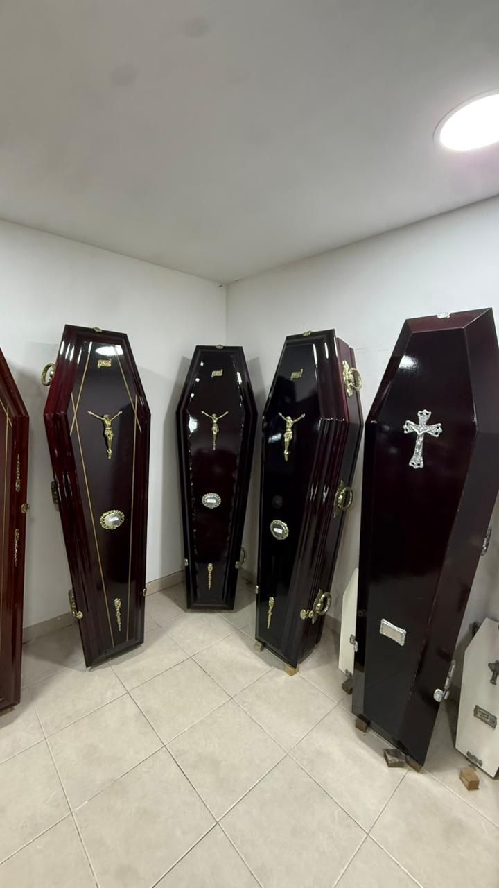 Ataúdes alineados en una pequeña habitación blanca con suelo de baldosas y luz en el techo.