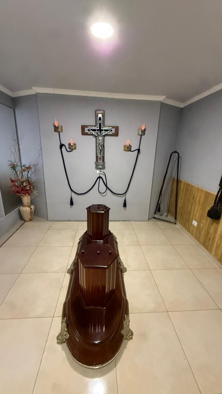 Habitación pequeña con un ataúd en el centro y una cruz colgada en la pared con velas detrás.
