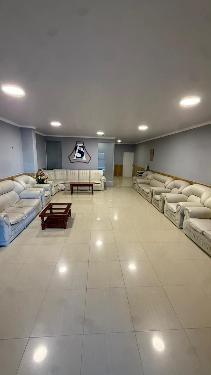 Amplia sala de estar con sofás beige, suelo de baldosas brillantes, luces empotradas y televisor montado en la pared.