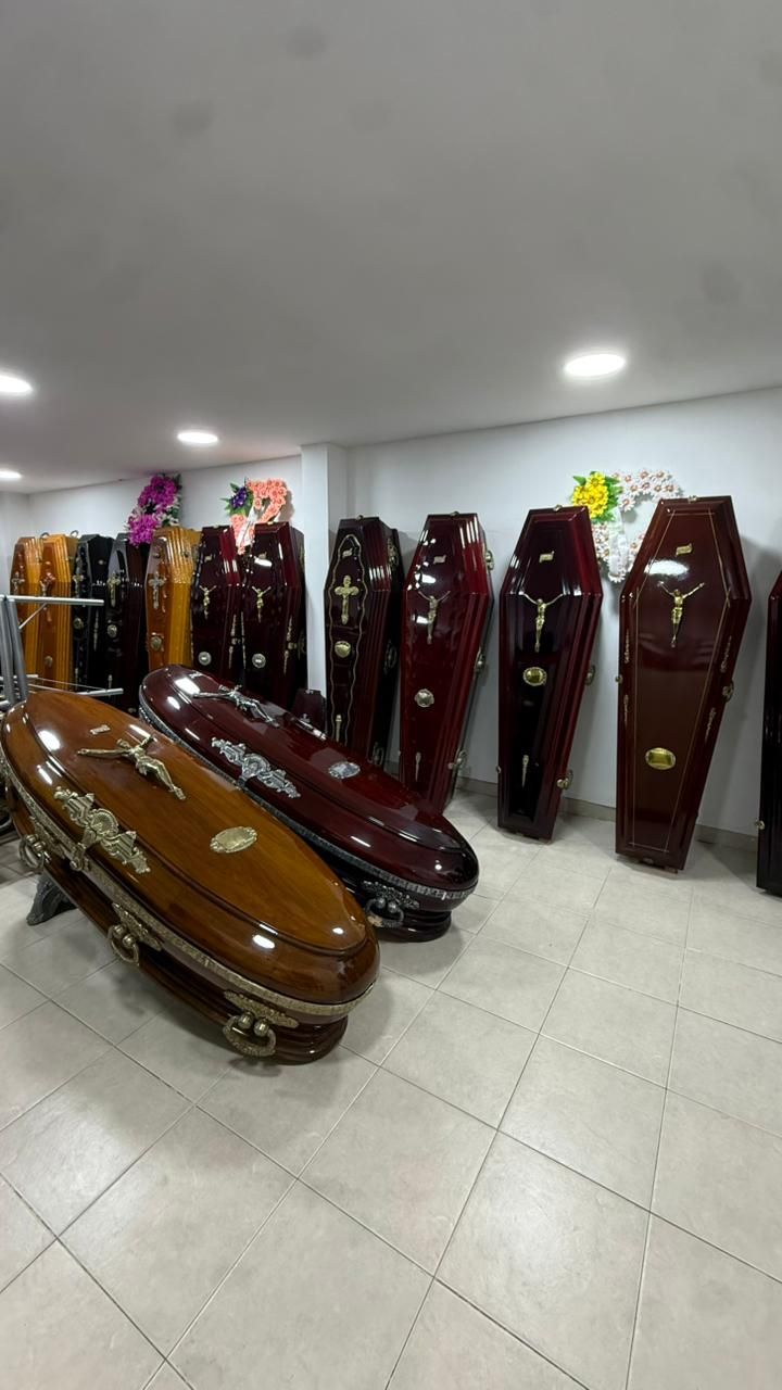 Filas de ataúdes color burdeos en una sala de exposición, con dos ataúdes marrones brillantes en primer plano.