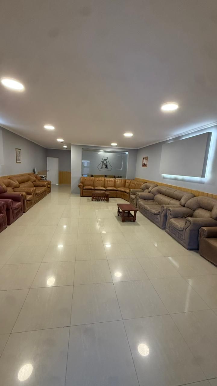 Amplia sala de estar con sofás, suelo de baldosas brillantes, luces empotradas y una gran ventana con persianas.