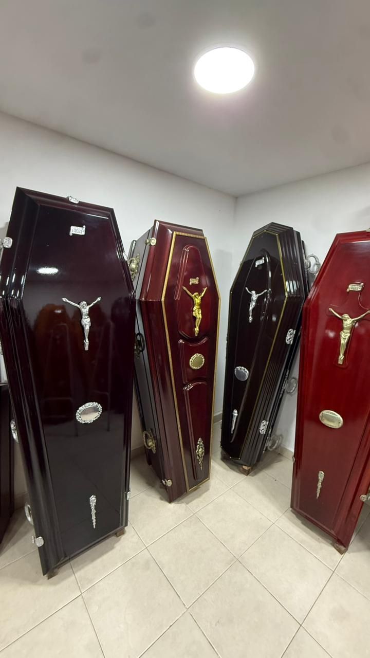 Cuatro ataúdes abiertos en una habitación blanca, dispuestos uno al lado del otro en acabados negros, burdeos, negros y rojos.