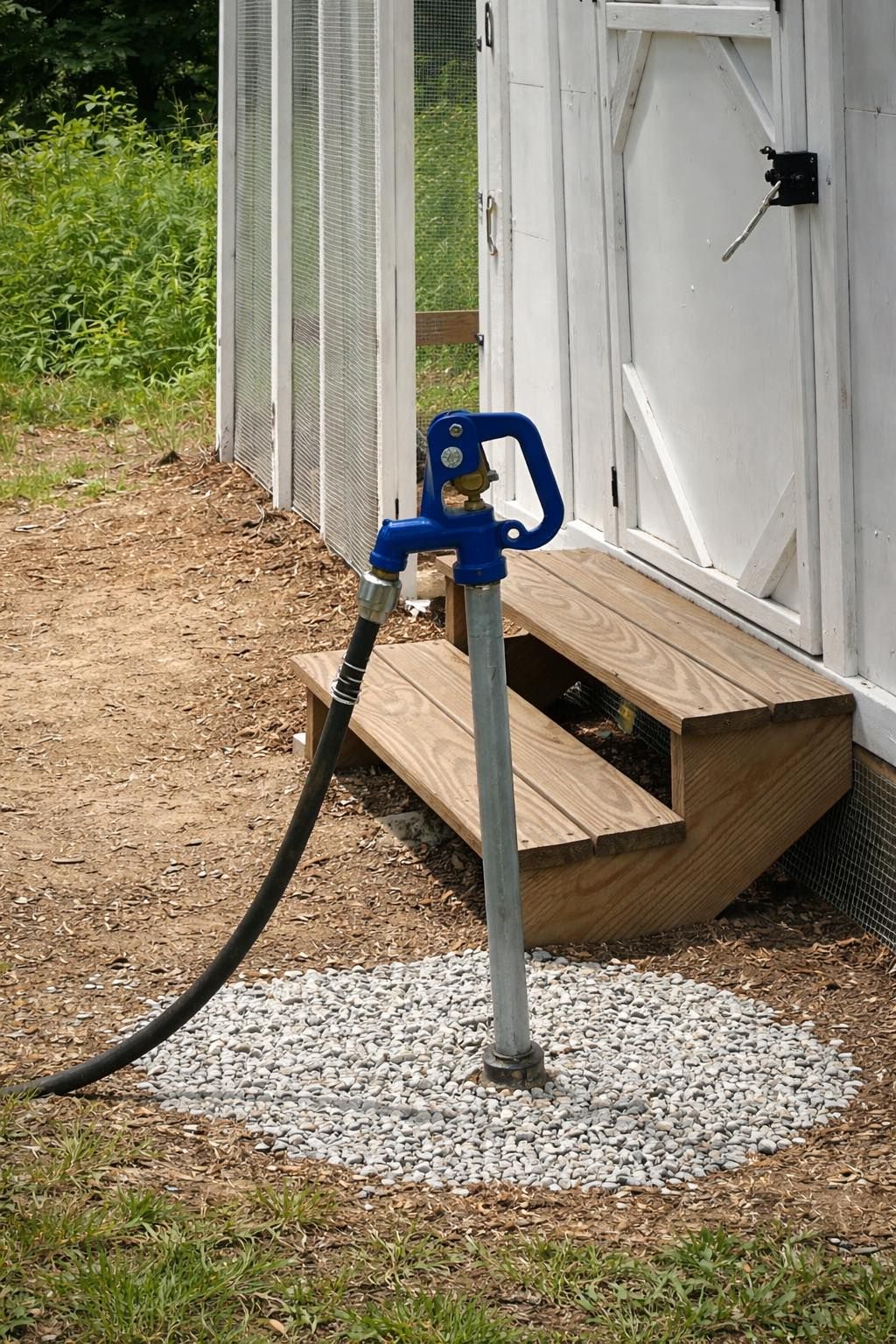 Blue water spigot on a metal post beside a white shed and wooden step on gravel.