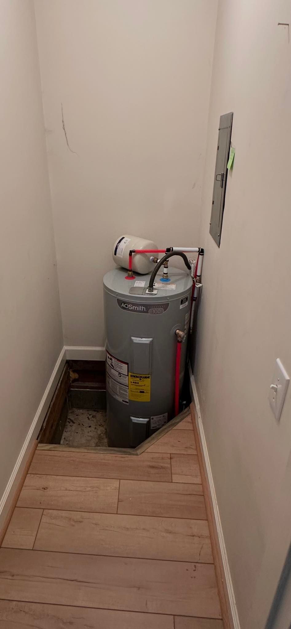 Narrow hallway with a large gray water heater at the end and wood flooring in the foreground.