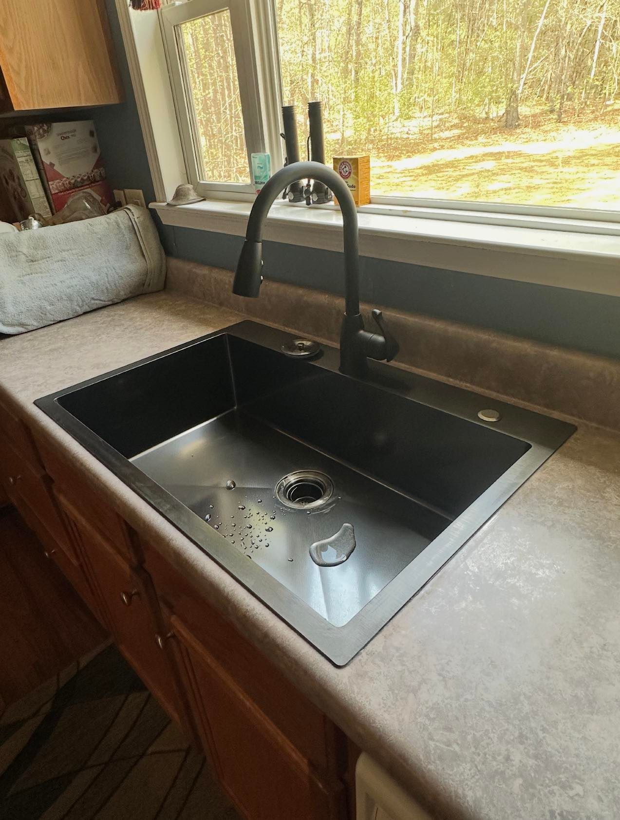 Kitchen sink beneath a window, with a matte black faucet and beige countertop.