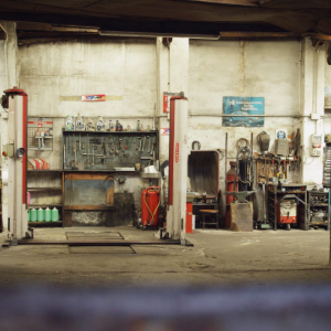 Industrial workshop interior with red machinery, metal workbenches, and tools against a worn wall.