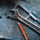 Metal wrench, ruler, and orange pencil on a dark workbench.