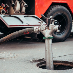 Fire truck water pump connection beside a wheel, with hose attached on a street.