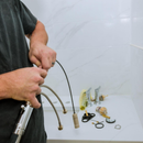 Plumber connecting hoses under a sink during faucet installation in a tiled bathroom