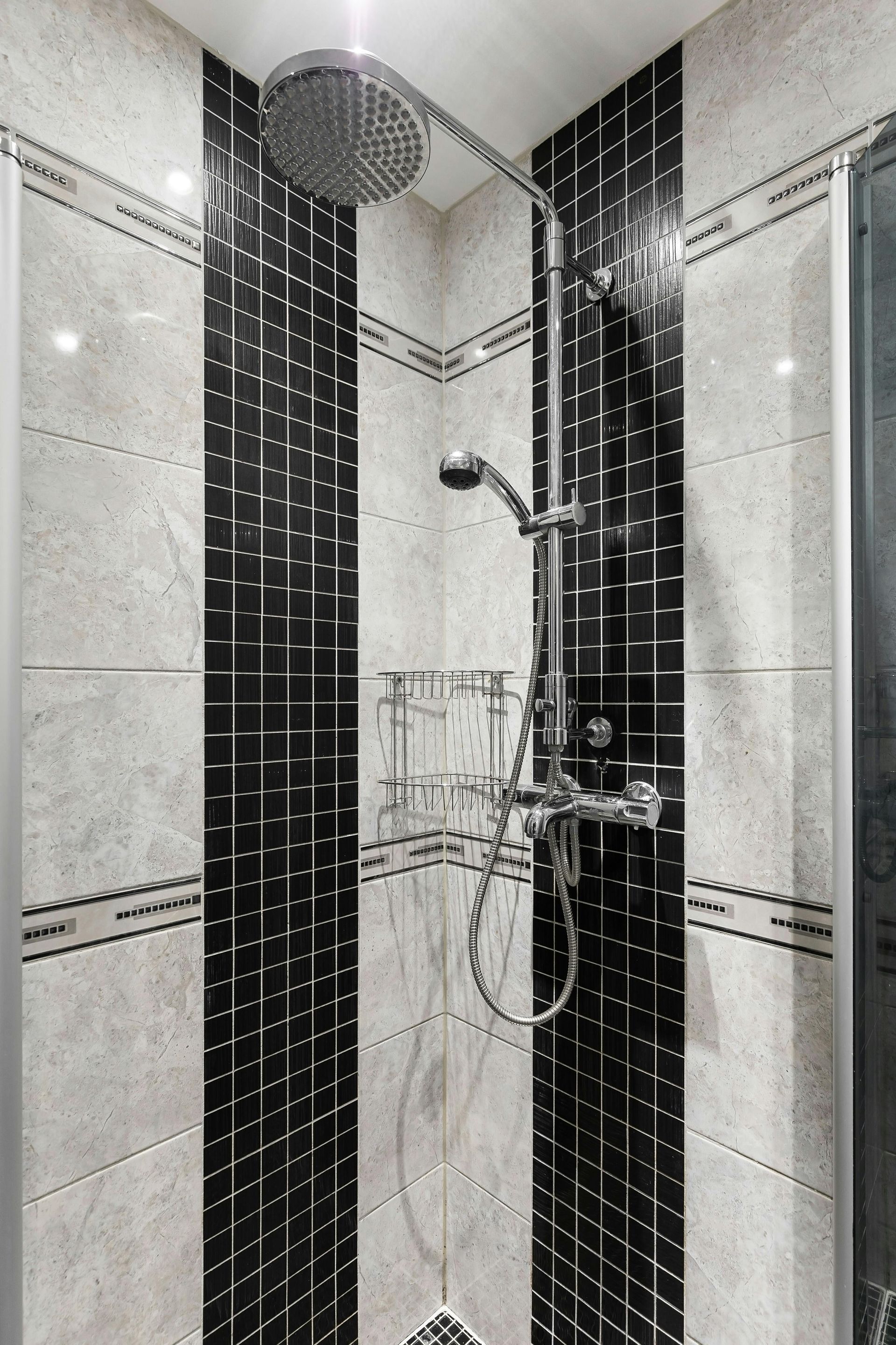 Modern tiled shower with rainfall showerhead, handheld sprayer, and black-and-white wall accents