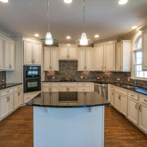 Spacious modern kitchen with cream cabinets, black countertops, island, pendant lights, and hardwood floors