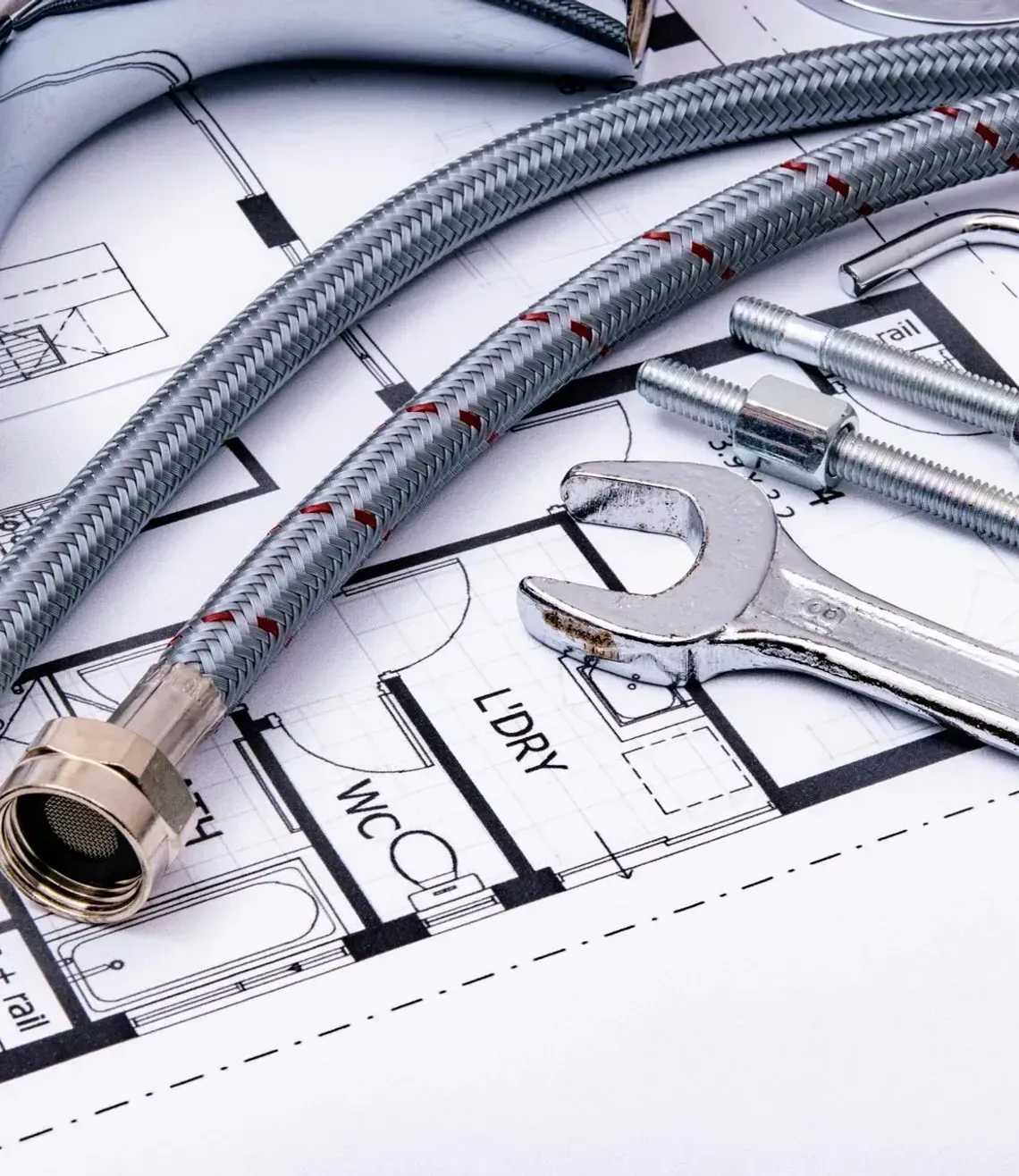 Chrome sink faucet hoses on plumbing blueprints, with wrench and fittings on a white surface