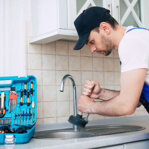 Plumber unclogging a kitchen sink with tools beside him