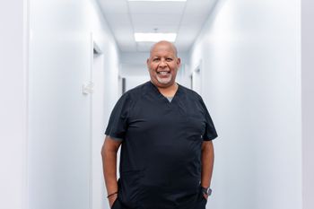 Man in black scrubs smiles in a white hallway with doors.