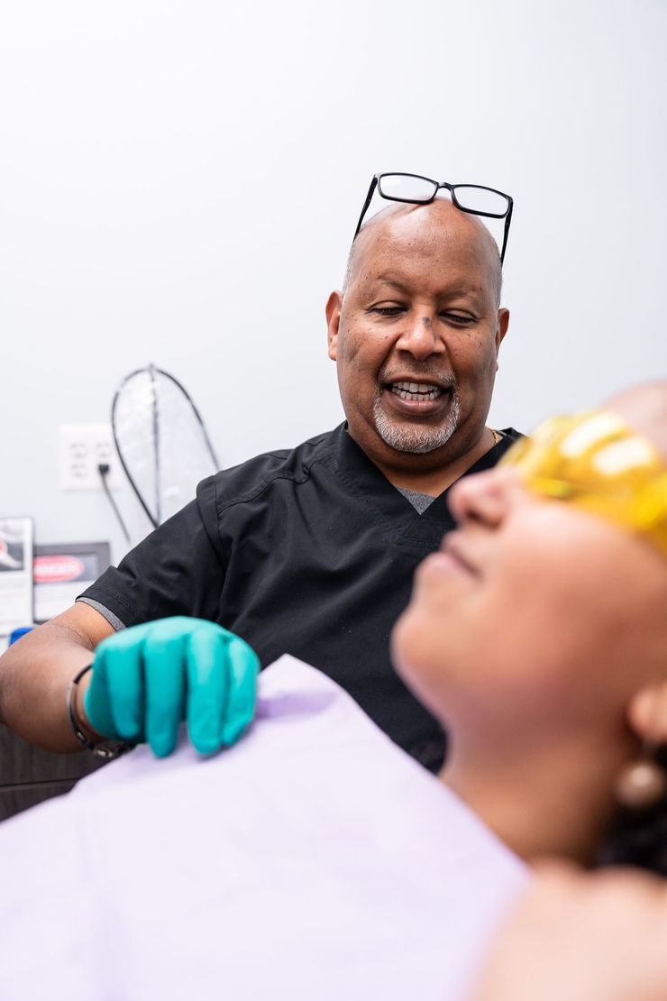 Dentist with glasses smiles at a patient in a dental chair.