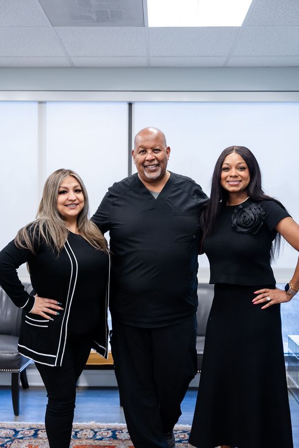 Three people posing together in an office. They are all wearing black clothing.