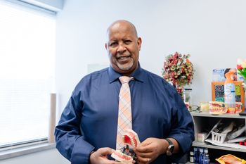 Man in blue shirt and tie holding dental models in an office.