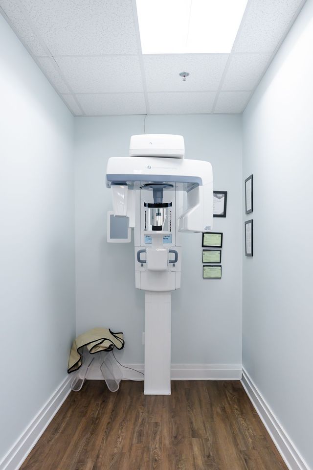 Dental panoramic X-ray machine in a small, light blue room with wood-look flooring.