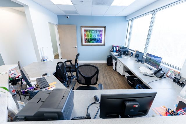 Reception area with a desk, computers, artwork, and a doorway.