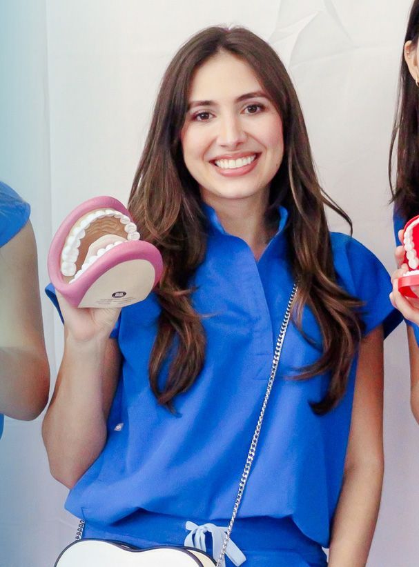 Woman in blue scrubs smiling, holding a model of teeth, white backdrop.