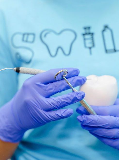 Dentist in blue gloves holding dental mirror and tooth model.