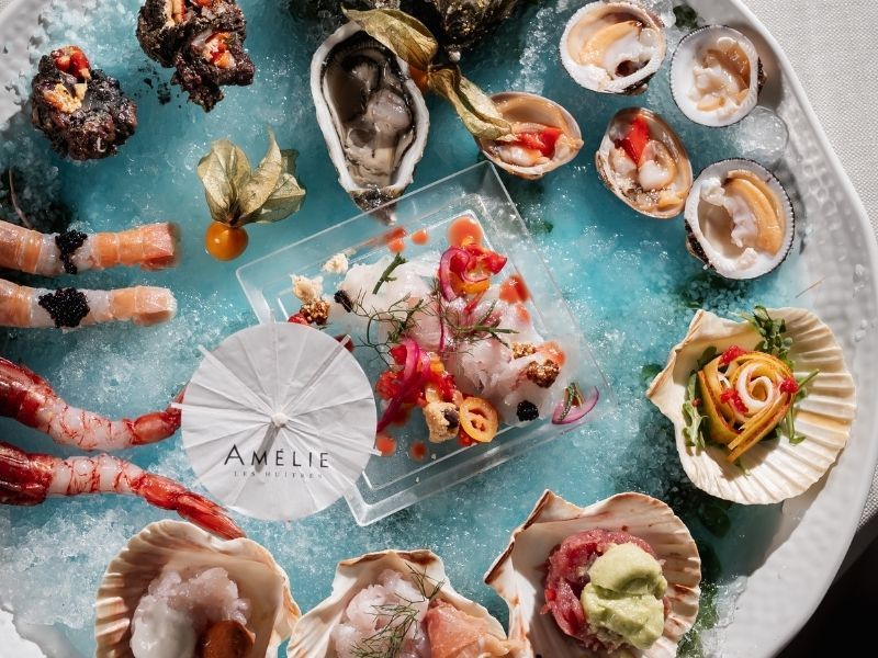 Assortimento di antipasti di pesce su un vassoio rotondo con cocktail e un centrotavola a forma di ombrellino bianco.