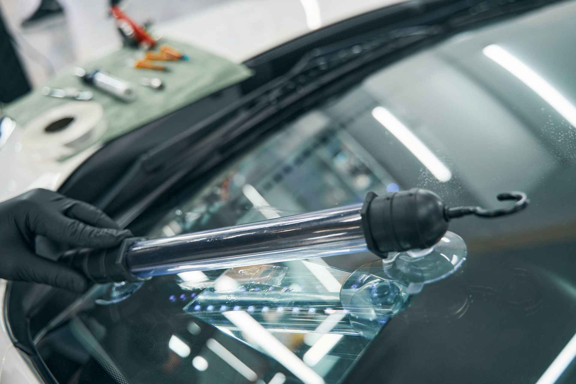 Person in black gloves using a repair tool on a car windshield.