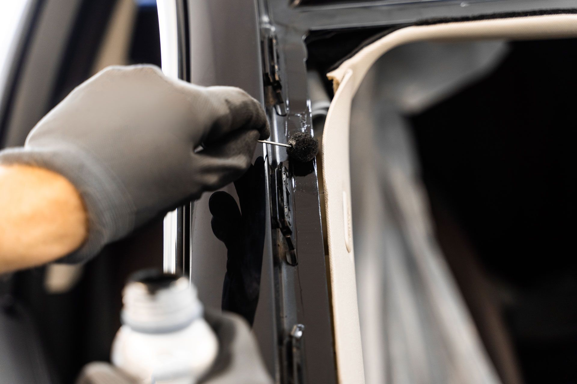 Person wearing black gloves applying sealant to a car door frame.