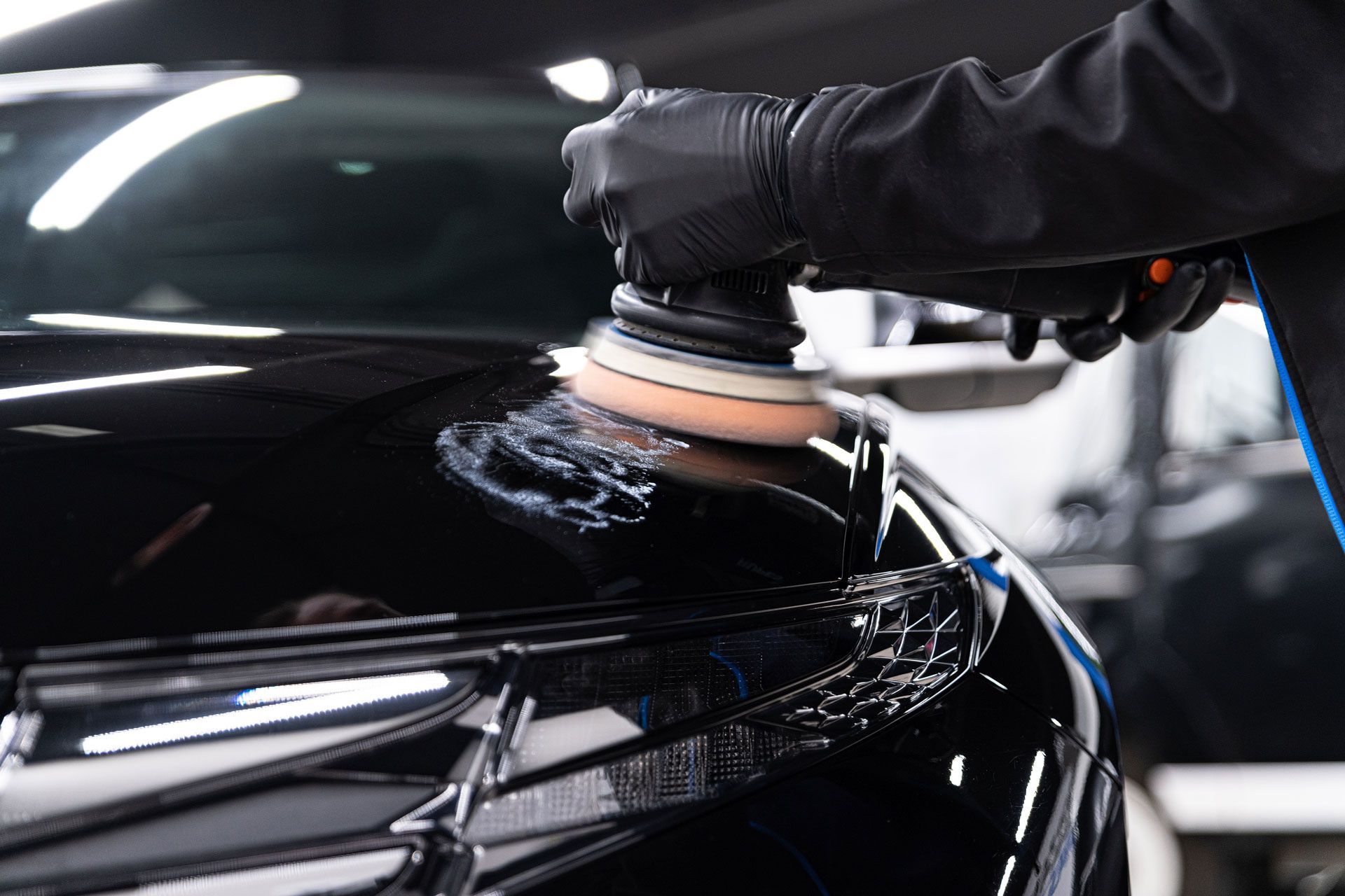 Black-gloved hands using a polisher on a black car hood.