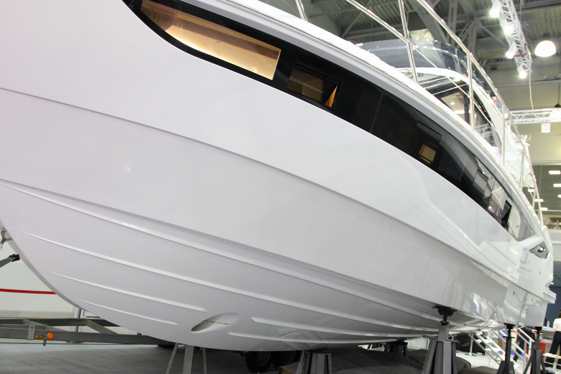 White motorboat hull, with horizontal lines and large windows, on display supports.