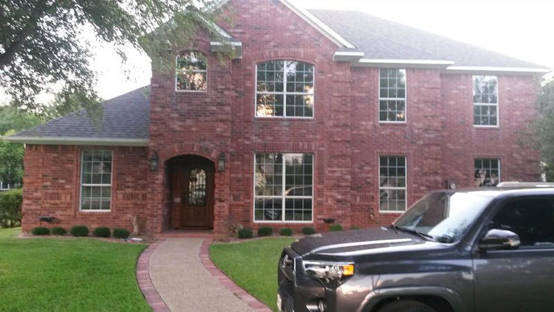 Red brick house with a pathway, landscaping, and a gray SUV parked in the front.