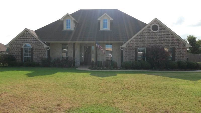 Brick house with dormers, shutters, and flag on a sunny day.