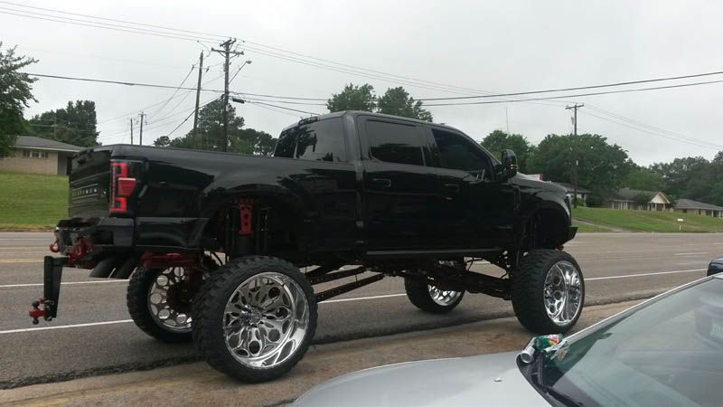 Black lifted pickup truck with large chrome wheels, red suspension, driving on a road.