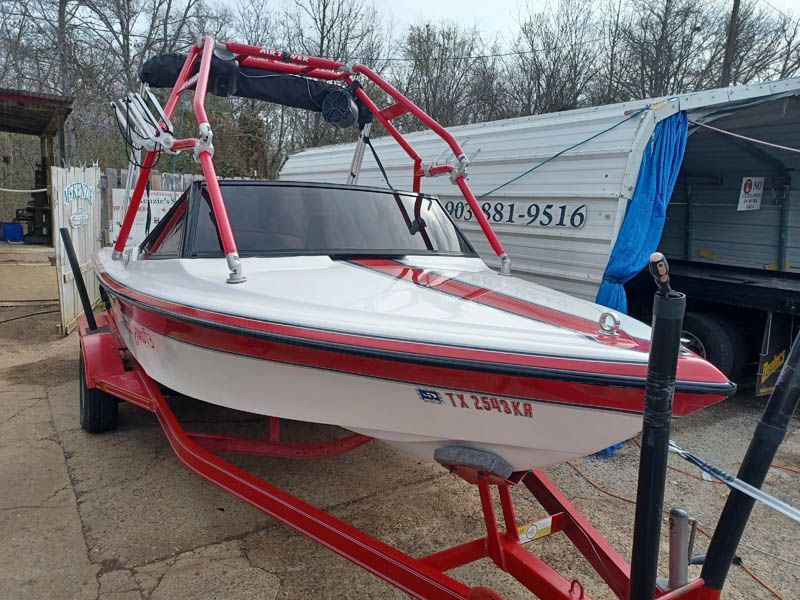 White and red boat on a red trailer with a red wakeboard tower; TX license plate.