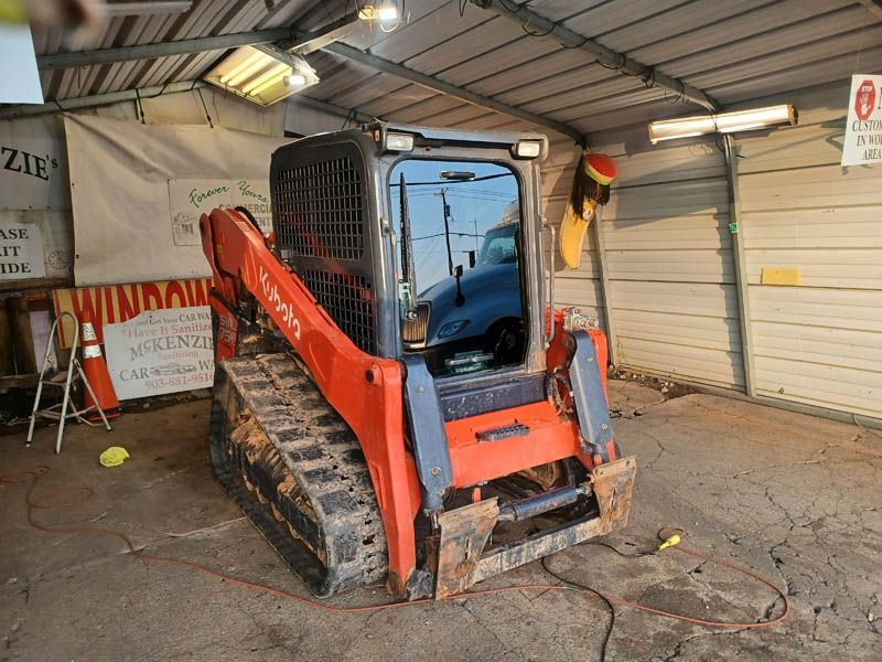 Orange and black Kubota track skid steer inside a garage with lighting and signage.