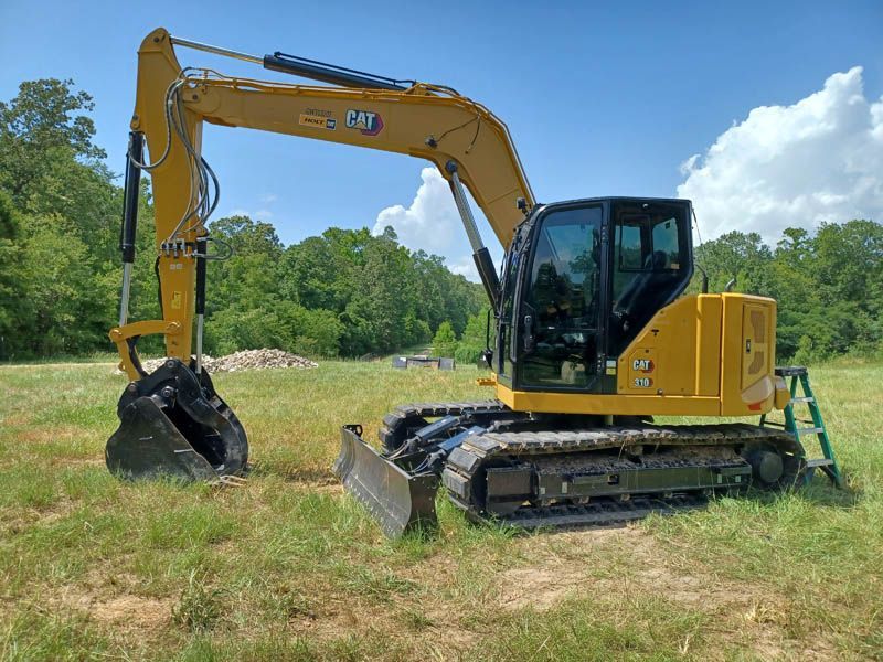 Yellow Caterpillar excavator parked on a grassy field with a dark bucket and blade.
