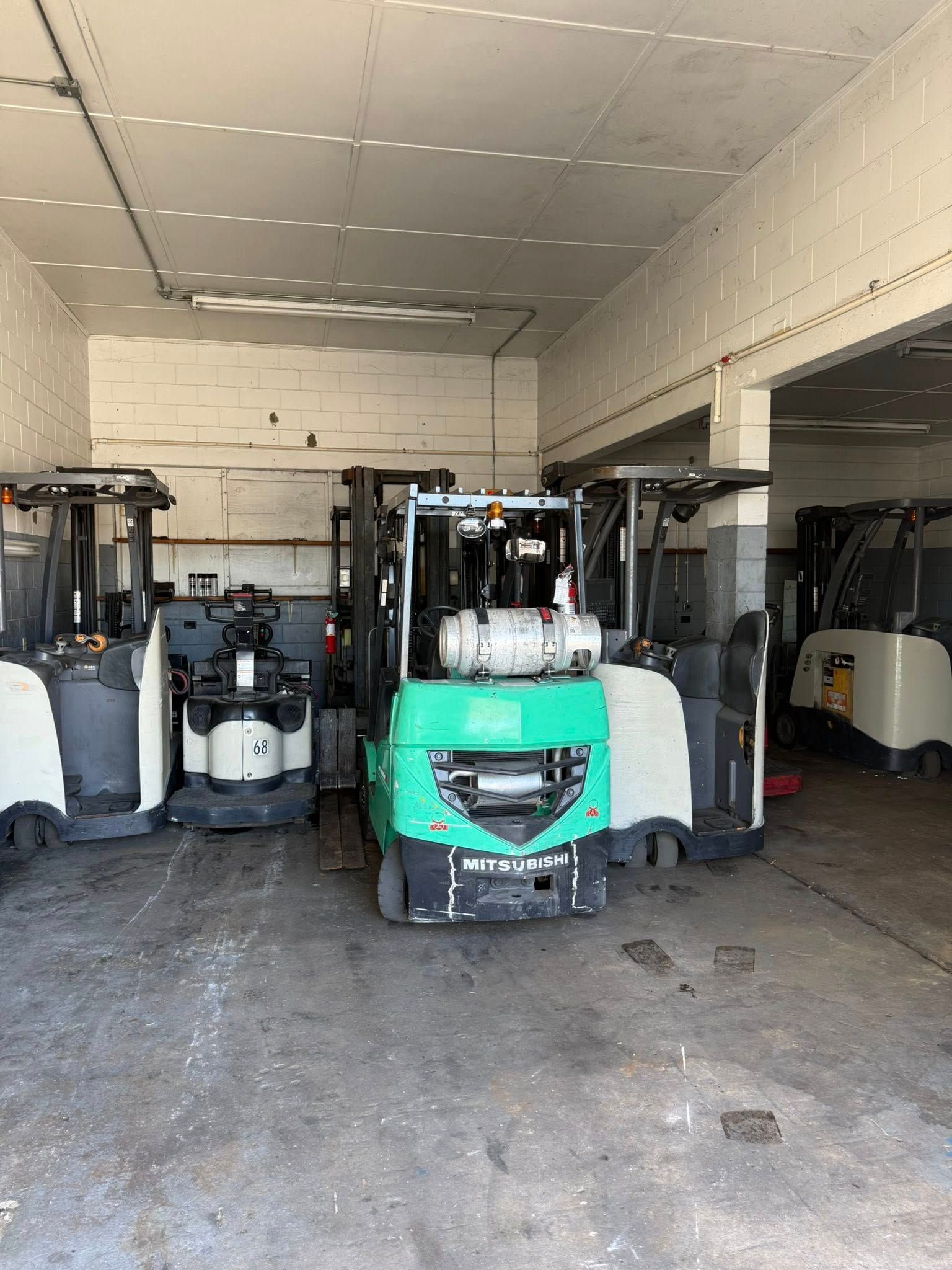 A warehouse interior with four forklifts parked in a row, featuring a prominent green unit in the center.