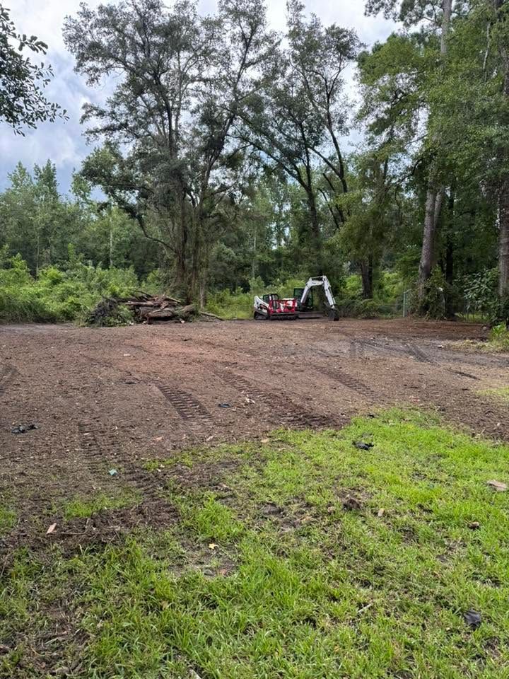 Cleared dirt lot with a small red excavator near trees in a wooded area