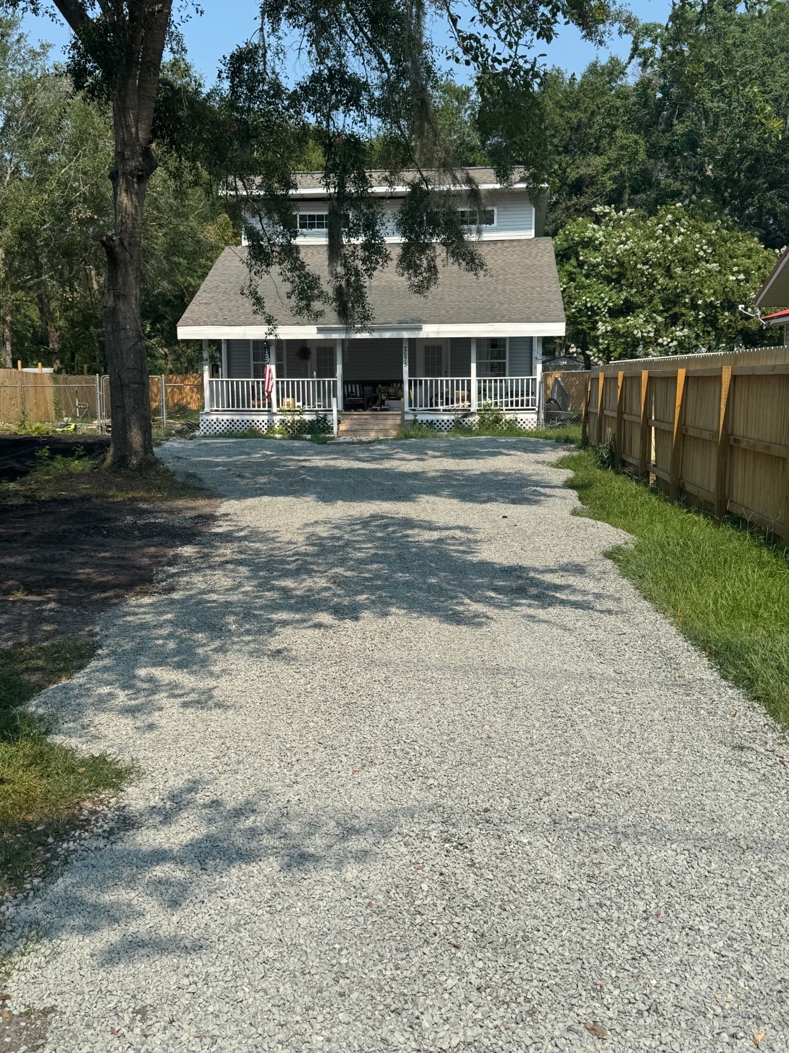 Gravel driveway leading to a white two-story house with a porch and trees in the yard