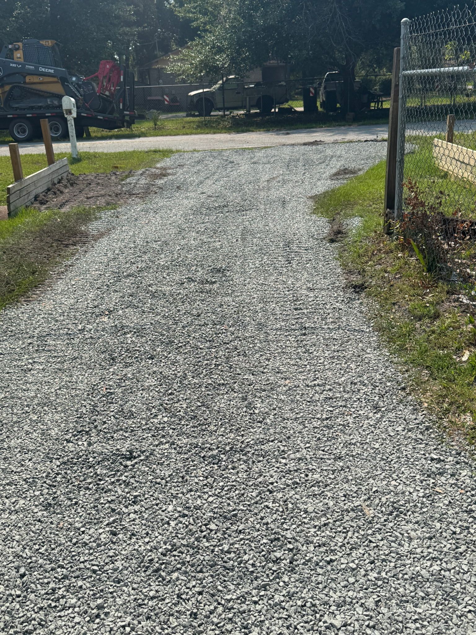 Gravel path leading to a sunlit garden gate with grass and trees on either side